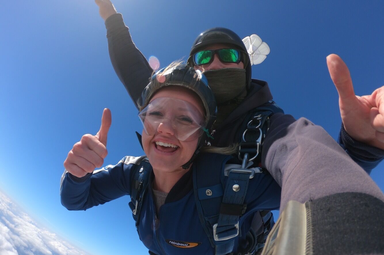 Nina Hundert und Sprungpartner lächeln während des Fallschirmsprung in die Kamera