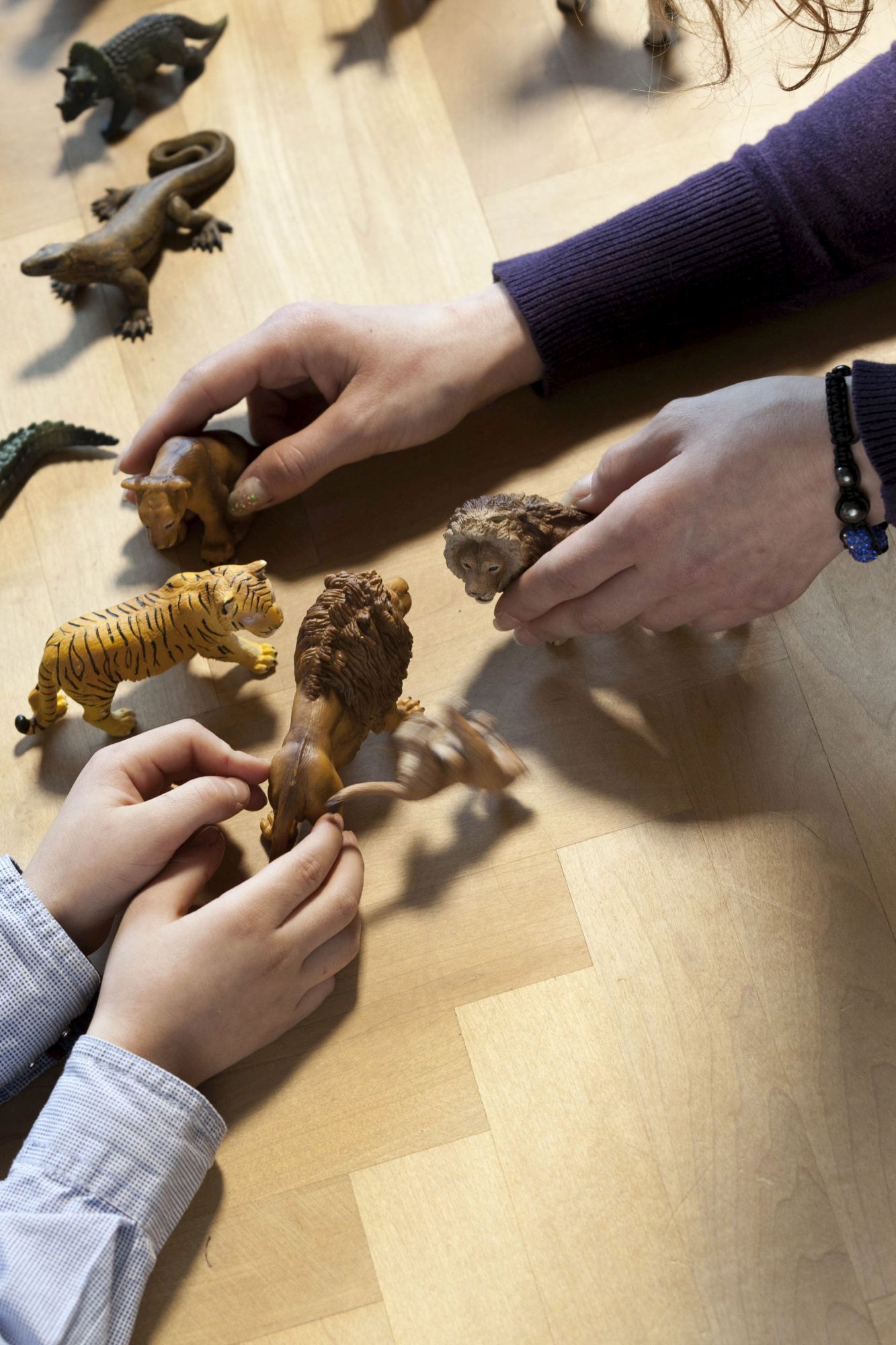 Erwachsene und kindliche Hände spielen mit Tier-Figuren
