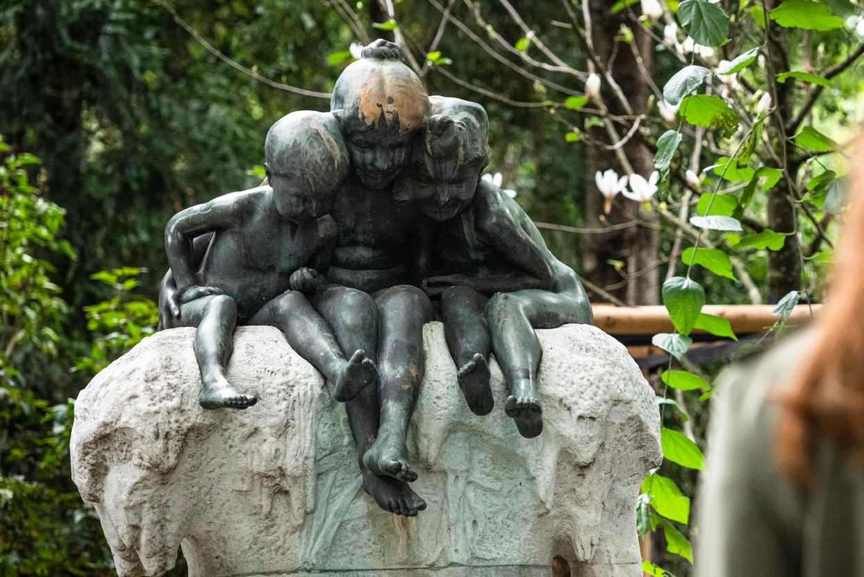 Eine junge Frau blickt auf eine Skulptur von einer Gruppe sich umarmender Kinder.