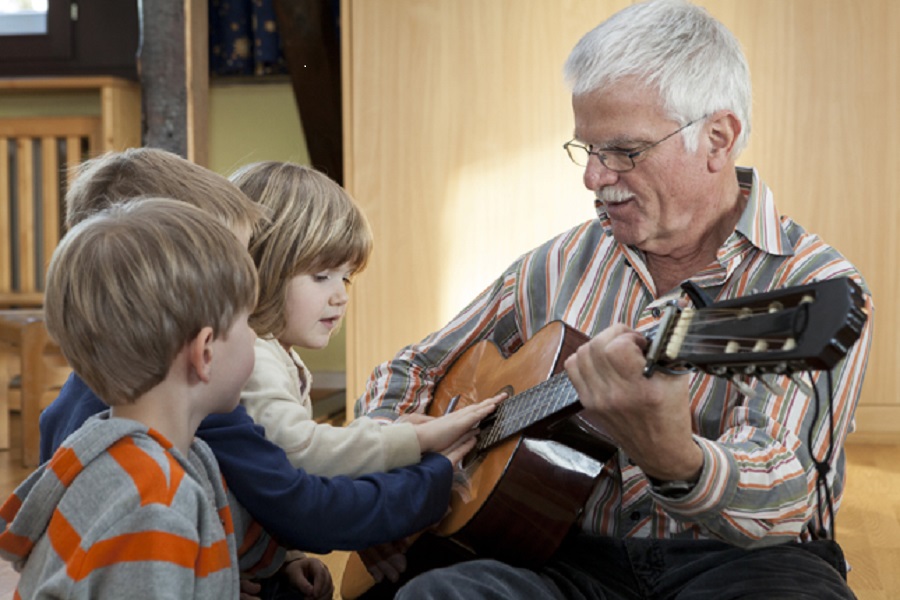 Ein Ehrenamtlicher spielt mit Kindern Gitarre