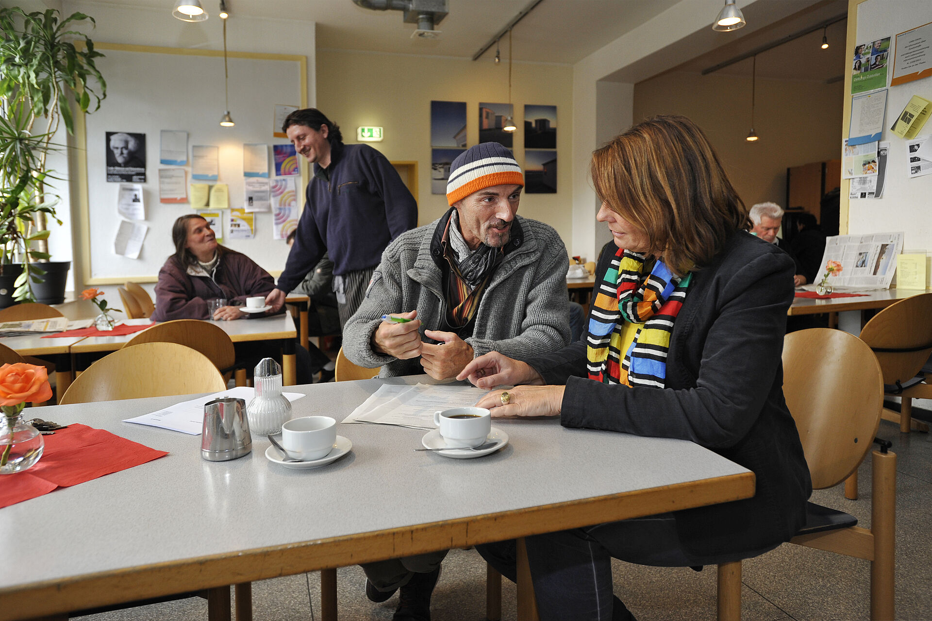 Eine Mitarbeiterin des Horizont berät einen wohnungslosen Menschen im Café. 