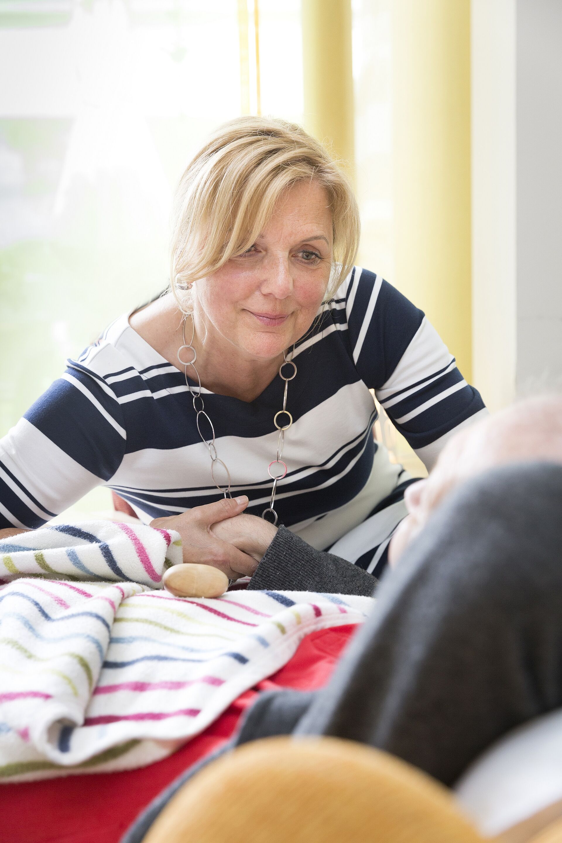 Jüngere Frau hält die Hand eines bettlägrigen Mannes