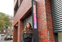 Frau vor Steinhaus mit Schild von "Welcome Point 02"