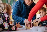 Zwei Kinder bauen mit ihren Eltern ein Lebkuchenhaus.