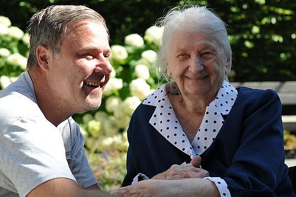 Ein Mitarbeiter der Diakonie und eine ältere Dame genießen die Sonne im Garten.