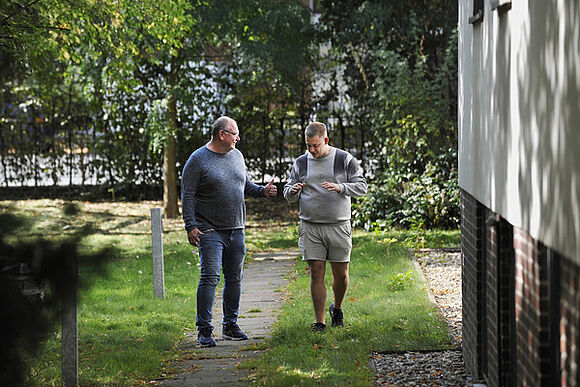Ein Mitarbeiter und ein Bewohner des Friedrich-Naumann-Hauses unterhalten sich bei einem Spaziergang durch den Garten des Naumann-Hauses. 