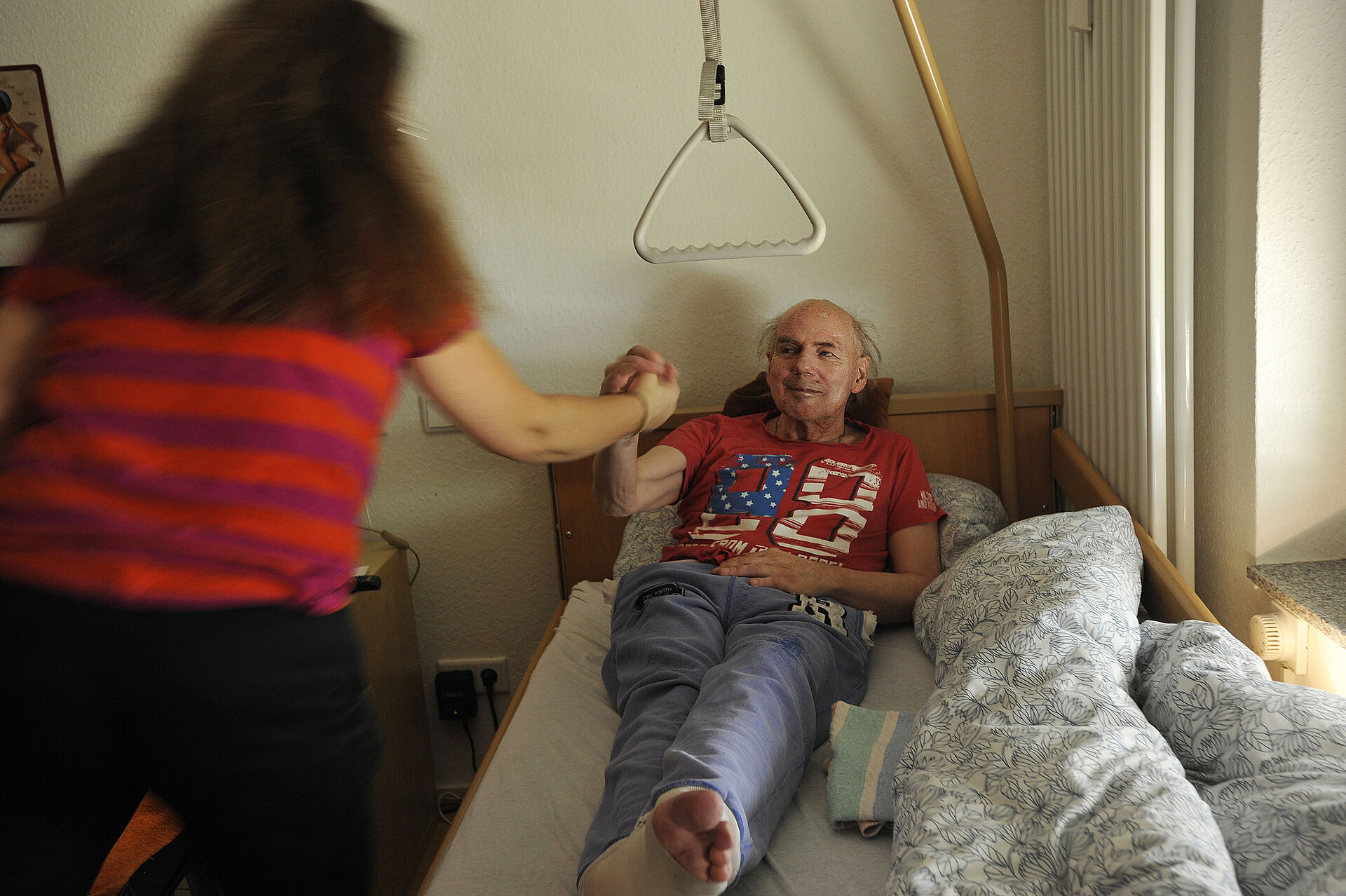 Aleksandra Wilczek-Konderak steht an einem Pflegebett, in dem ein Mann liegt.