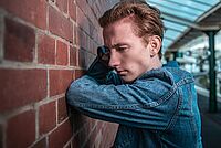 Ein junger Mann lehnt nachdenklich an einer Wand
