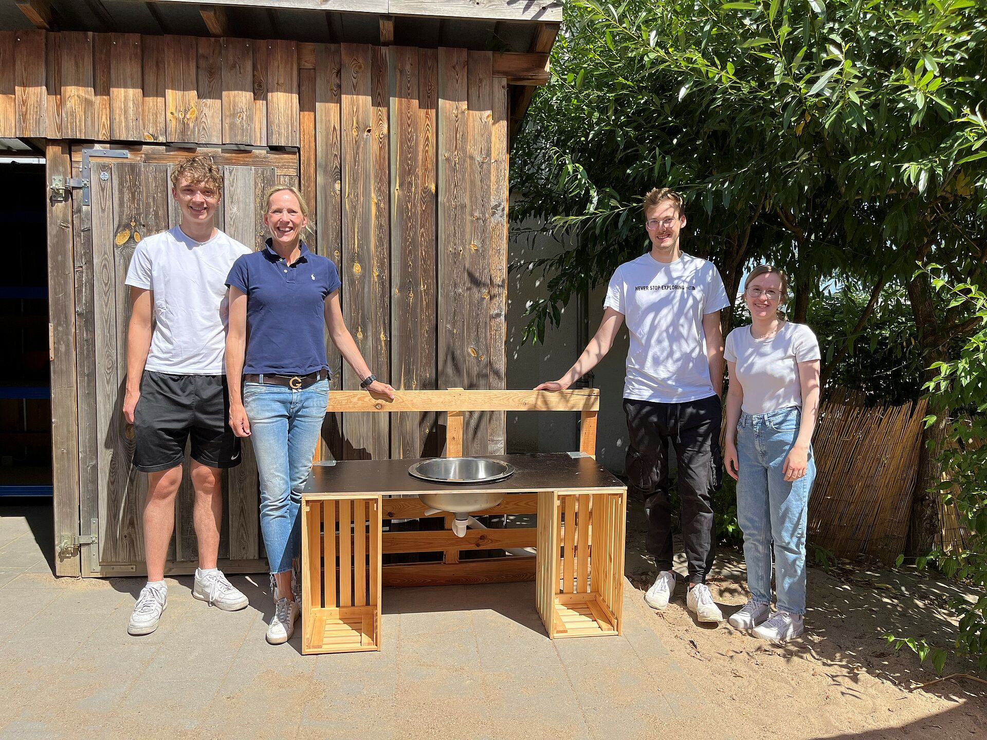 4 ehrenamtliche Helfer stehen um die selbstgebaute Matschküche im Kita-Garten