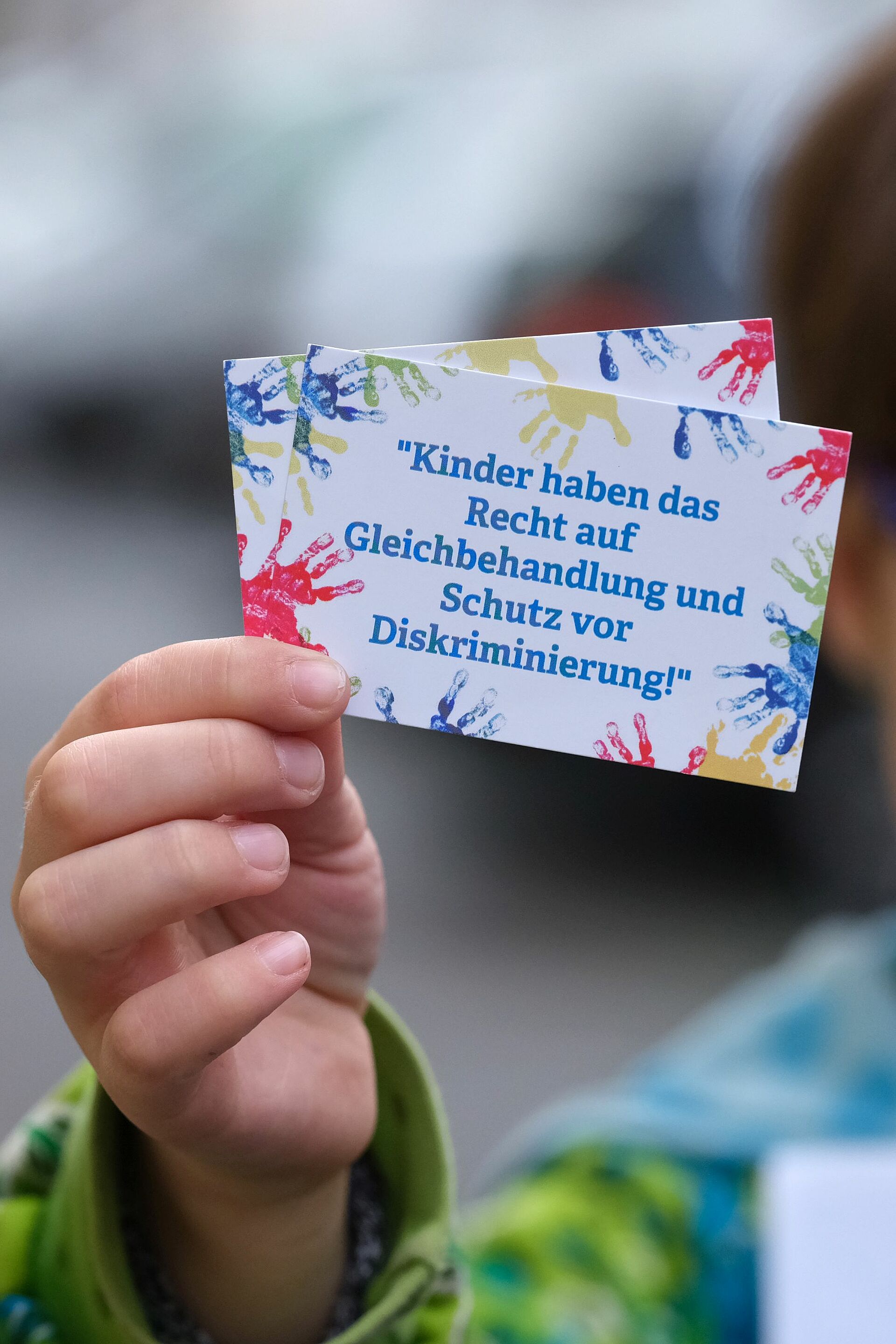 Kinderhand hält Schild hoch mit der Aufschrift "Kinder haben das Recht auf Gleichbehandlung und Schutz vor Diskriminierung"