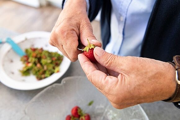 Eine Mitarbeiterin der häuslichen Pflege putzt Erdbeeren für eine Klientin. 