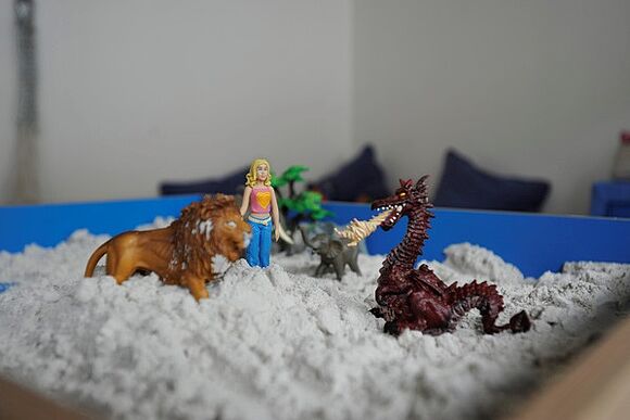 Spielfiguren stehen auf einem Sandberg. Zu sehen sind ein Drache, ein Löwe und ein kleines Mädchen. 